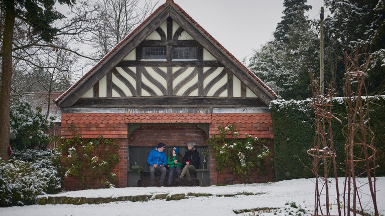 A family sitting on the bench in the snow in the formal garden at Wightwick Manor and Gardens.